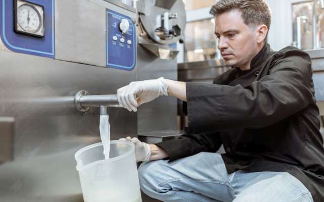 Mann, der Milch aus einem Pasteurisierer einschenkt